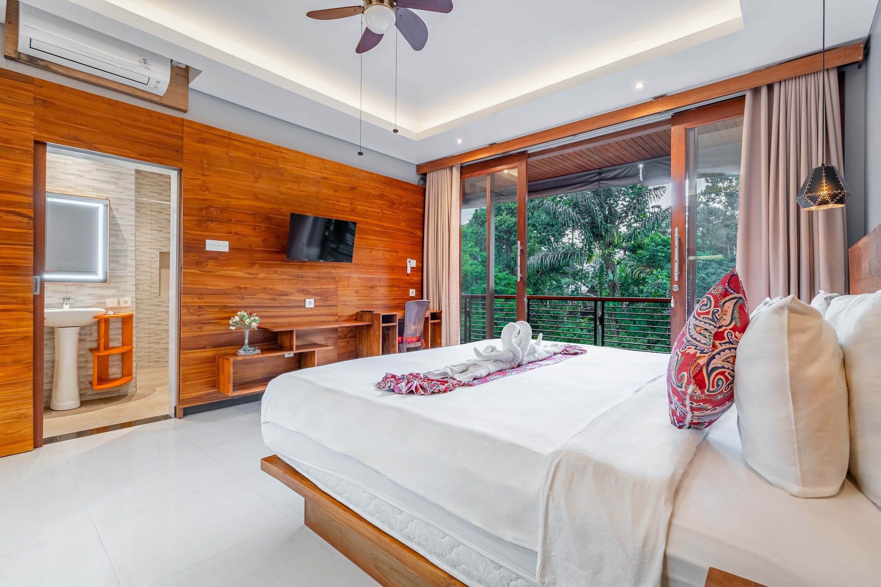 Une chambre d’hôtel moderne dotée d’un grand lit, de lambris en bois, d’une télévision, d’un balcon avec vue sur la verdure et d’un ventilateur de plafond.