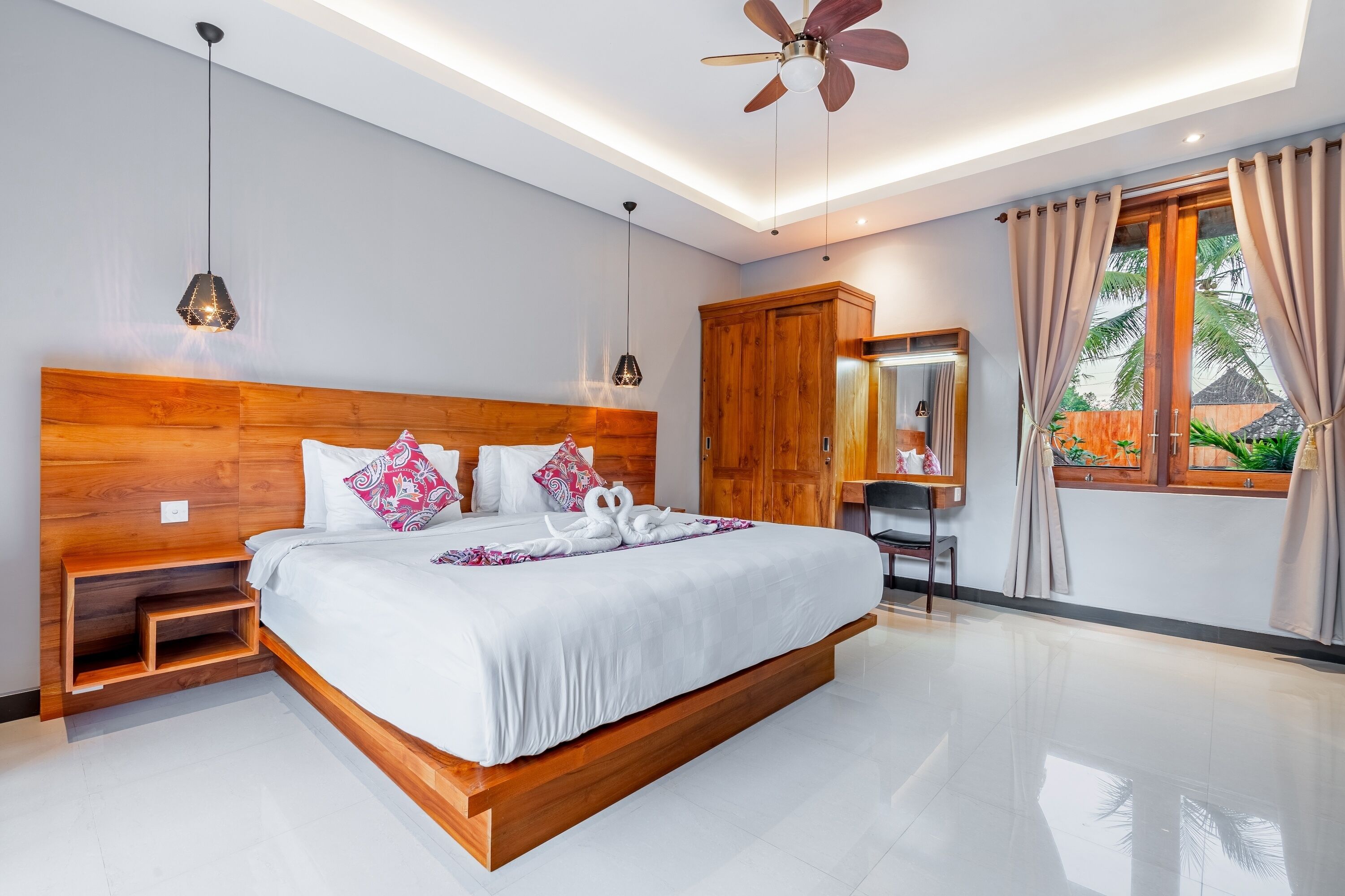 A modern bedroom with a wooden headboard, a large bed, a ceiling fan, and a window with curtains.