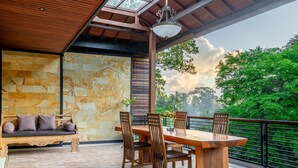 A wooden dining table with chairs, a wooden bench with cushions, and a stone wall with carvings. - Maru Fortuna Villa by Aayan (Gianyar)