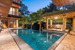 Een modern huis met een zwembad, houten terras en een zitgedeelte buiten.