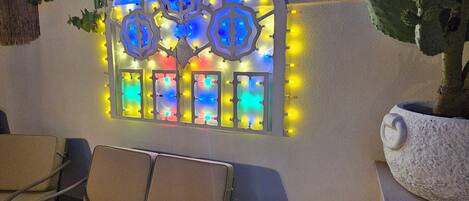 Un patio con una zona de estar con cojines, una pequeña mesa redonda e iluminación decorativa en la pared.