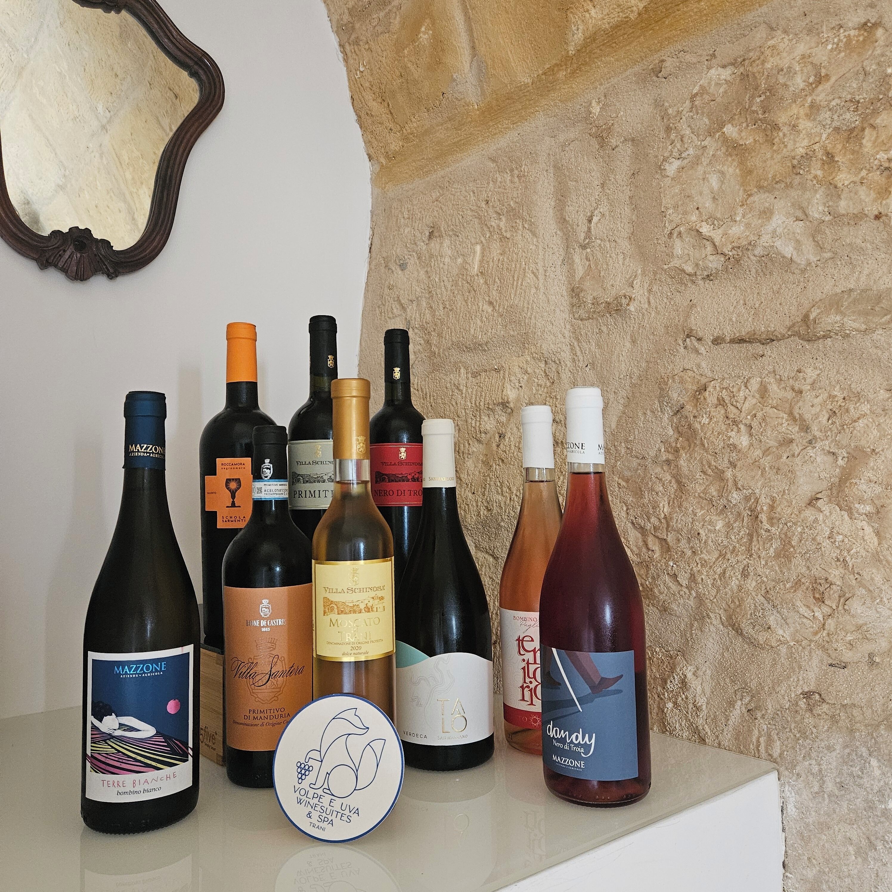 A selection of wine bottles on a table against a stone wall backdrop.
