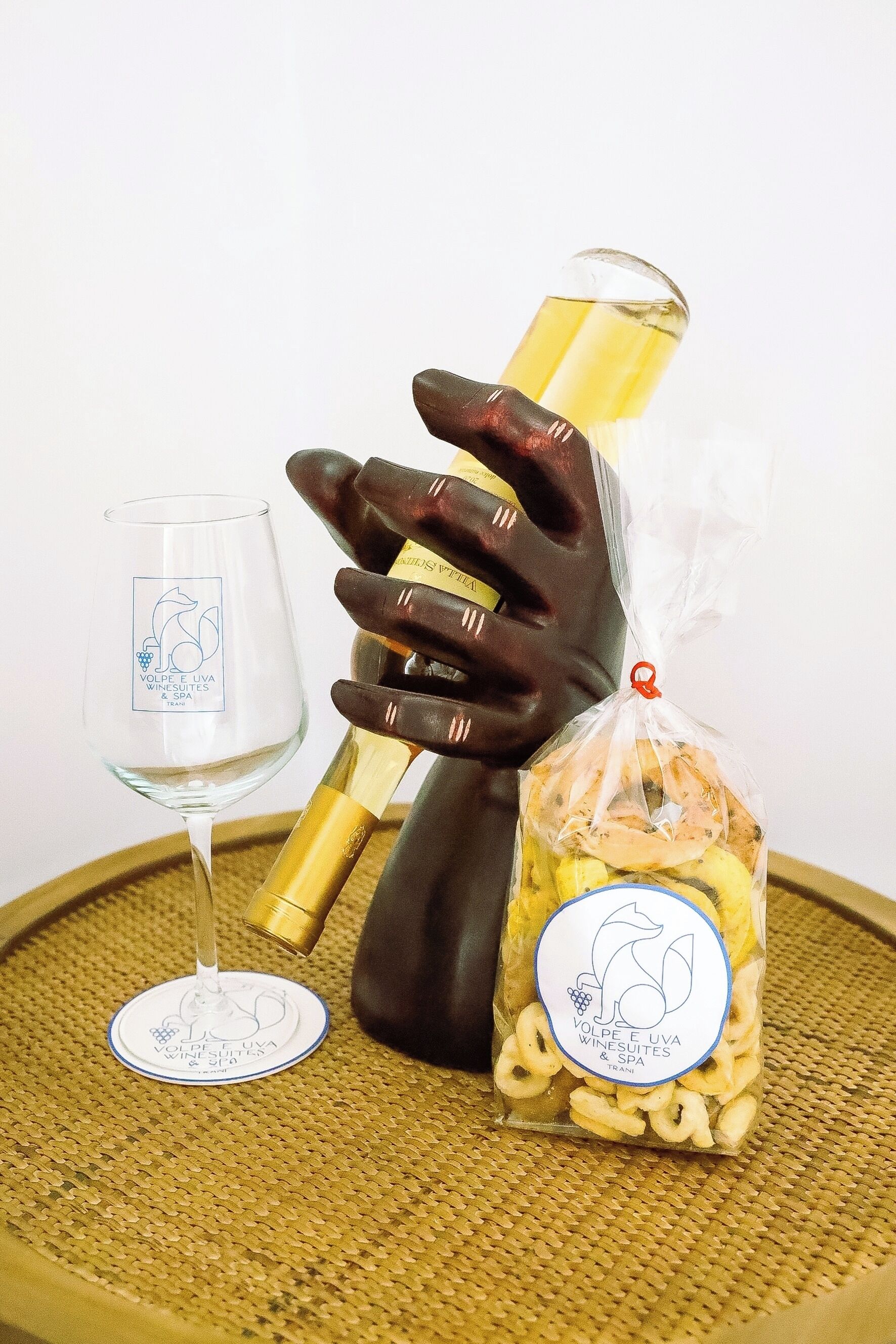 Un verre à vin, une bouteille et un sac de collations posés sur une surface tissée.
