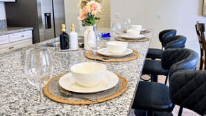 Een keuken met een granieten aanrecht, een vaas met bloemen en een eethoek met stoelen en borden.