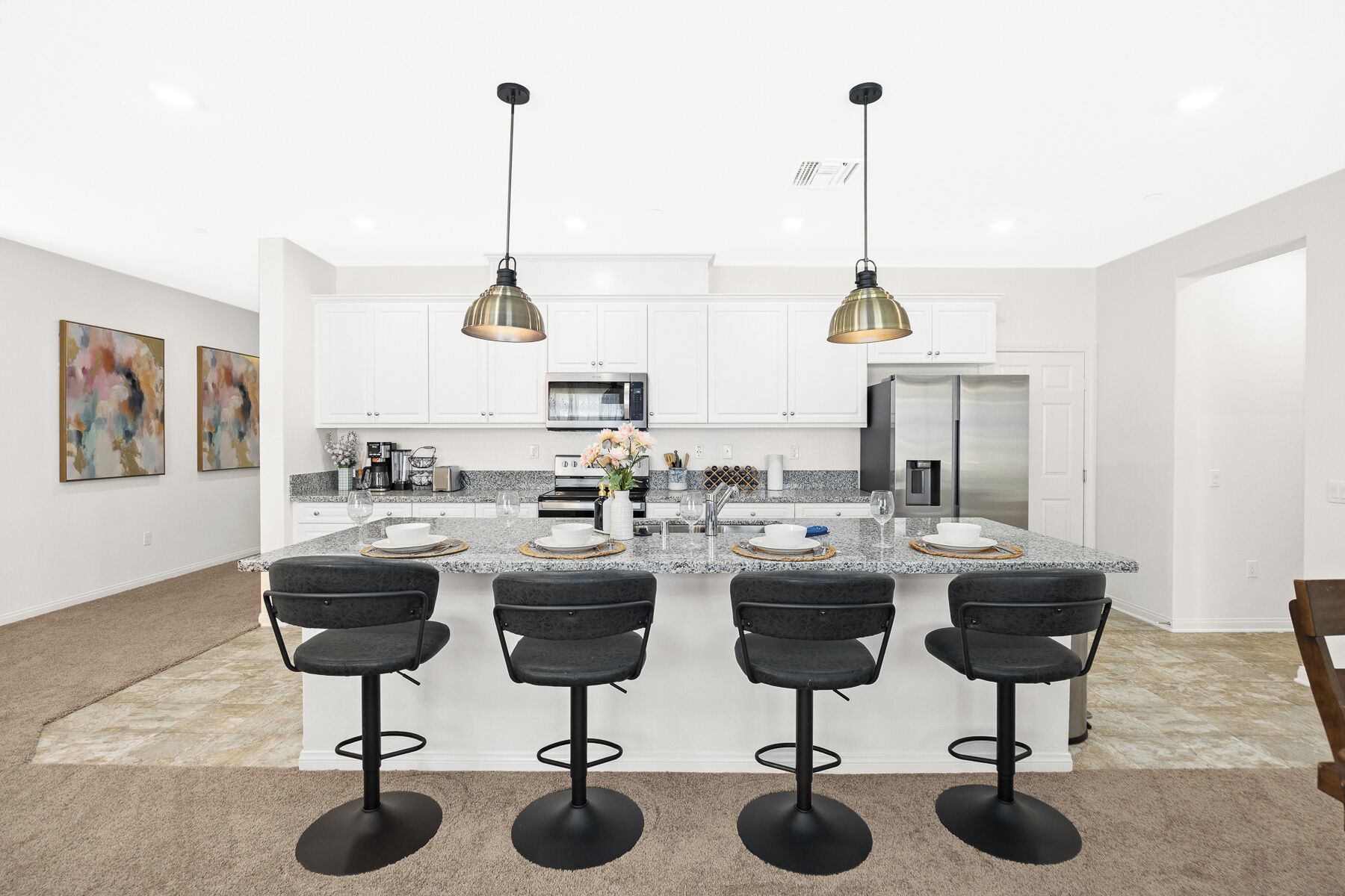 A modern kitchen with white cabinets, a central island with bar stools, stainless steel appliances, and pendant lighting.