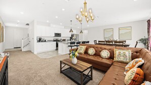 Een moderne woonkamer met een bruine leren bank, een houten salontafel en een eethoek met een tafel en stoelen.