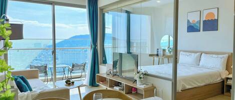 A hotel room with a balcony, a bed, a dining area, and a TV.
