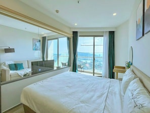A hotel room with a large bed, a sofa, a television, and a view of the city. - T-A Homes - The Sóng Aparment Vũng Tàu (Ho Chi Minh City)