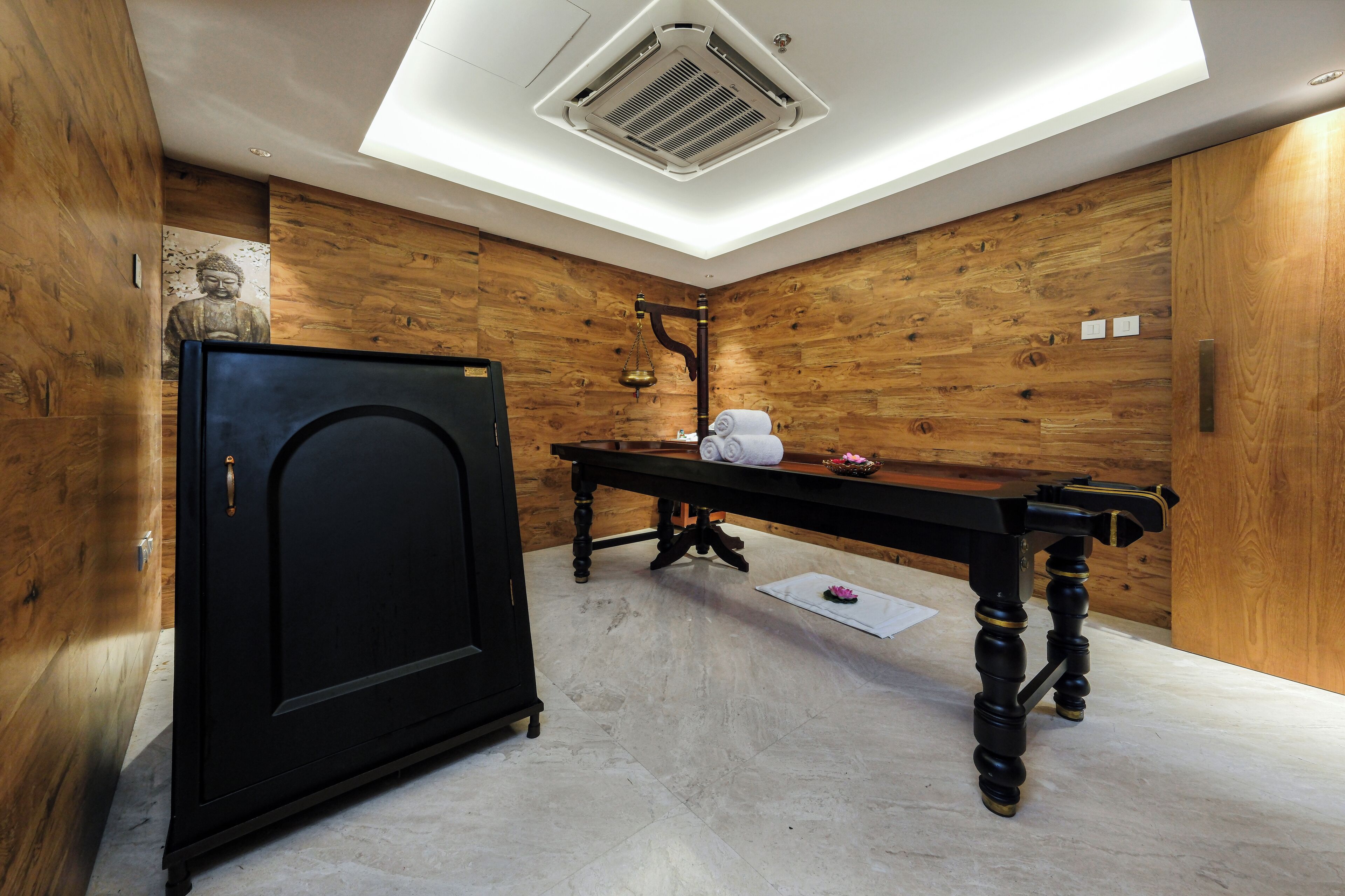 A room with wooden panel walls, a black cabinet, a wooden table with towels, and a ceiling vent.