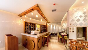 A modern bar area with wooden accents, a counter with stools, and a dining area with chairs. - TIARA BY MPS (Kozhikode)