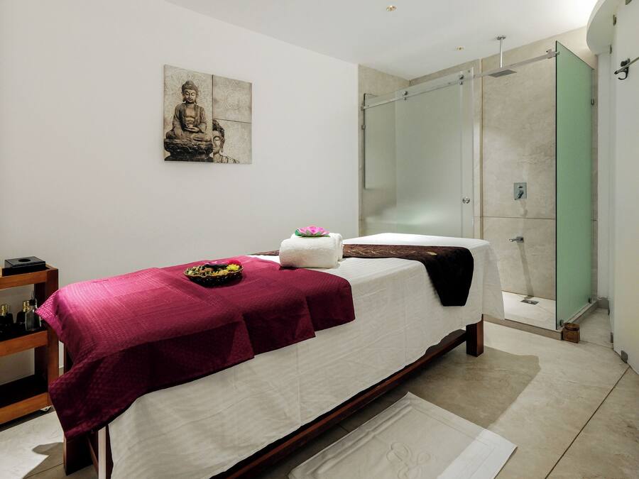 A modern bedroom with a bed, a glass shower enclosure, and a Buddha statue on the wall.