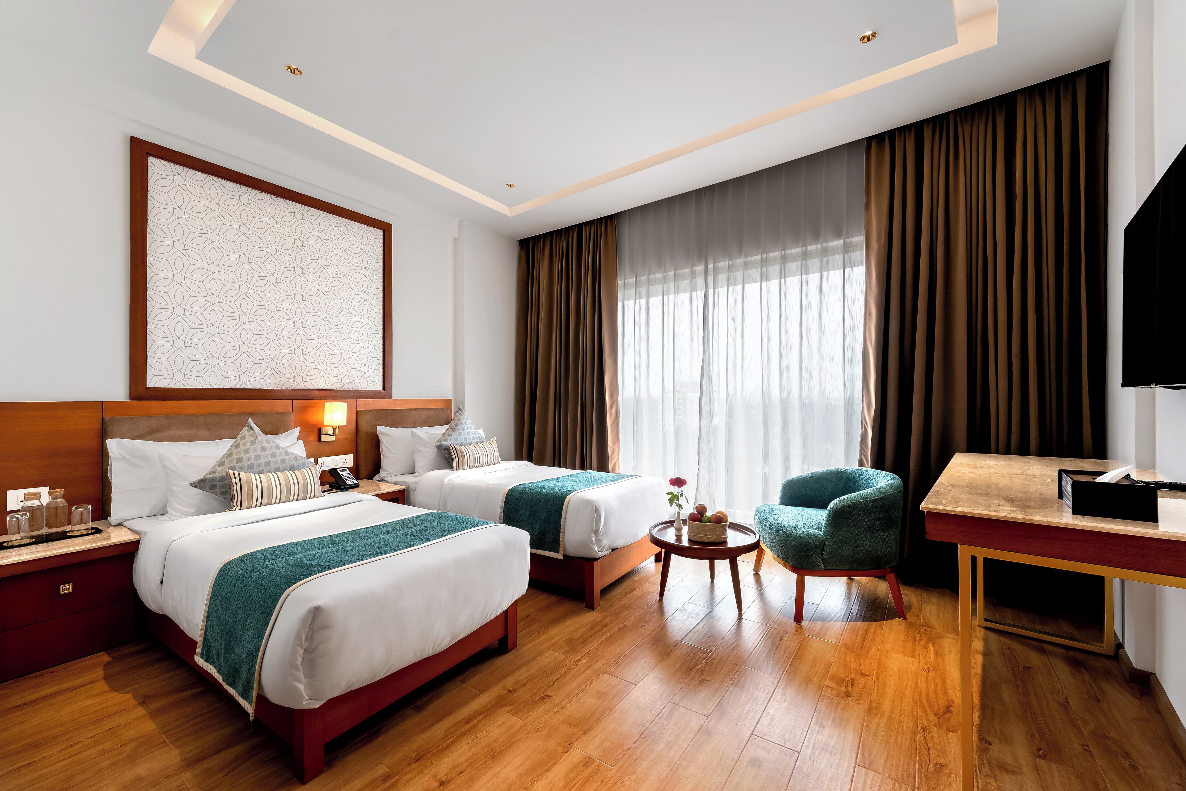 Habitación de hotel con dos camas, un escritorio, una silla y un ventanal con cortinas.