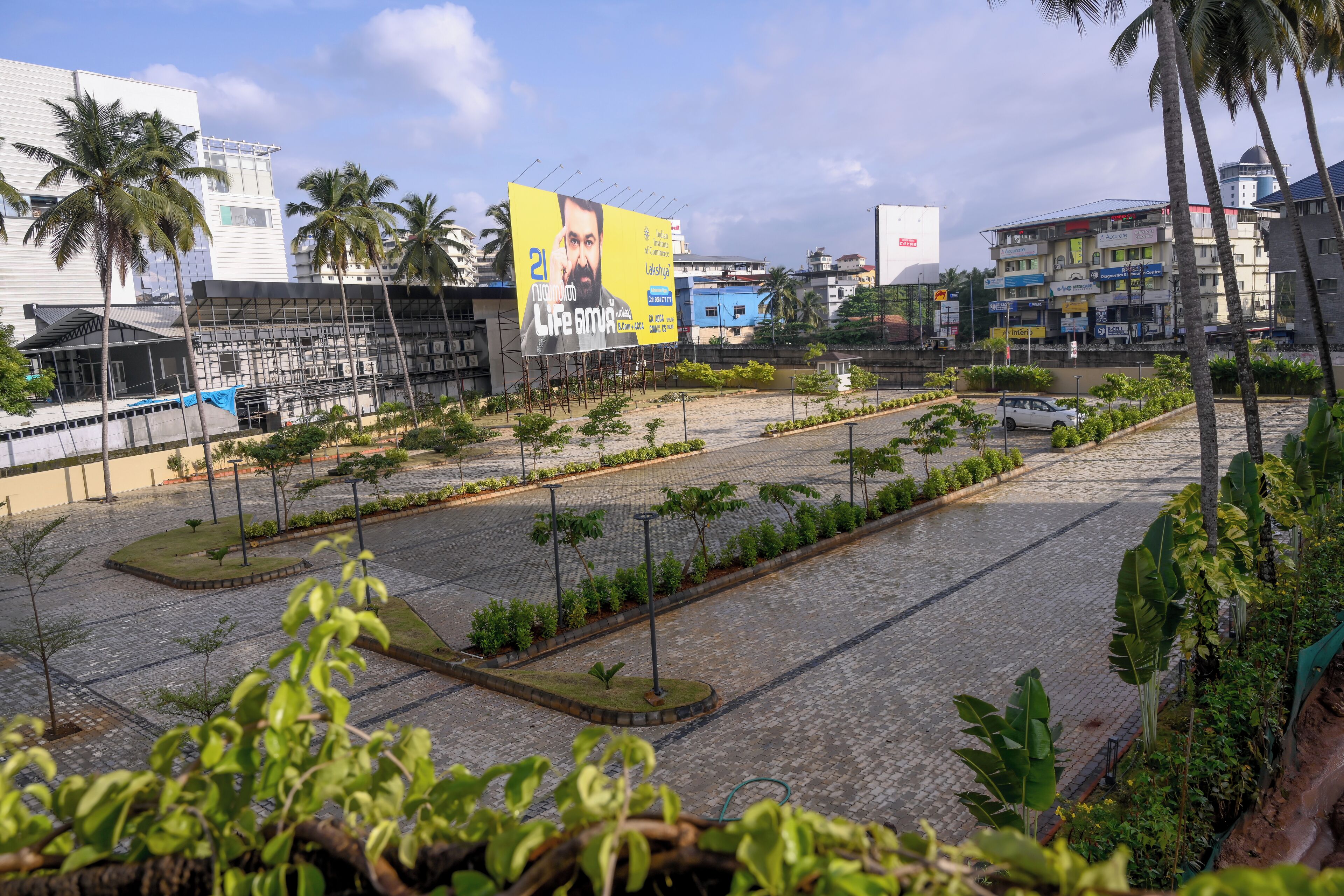 A paved plaza with palm trees, a car, and a large billboard.