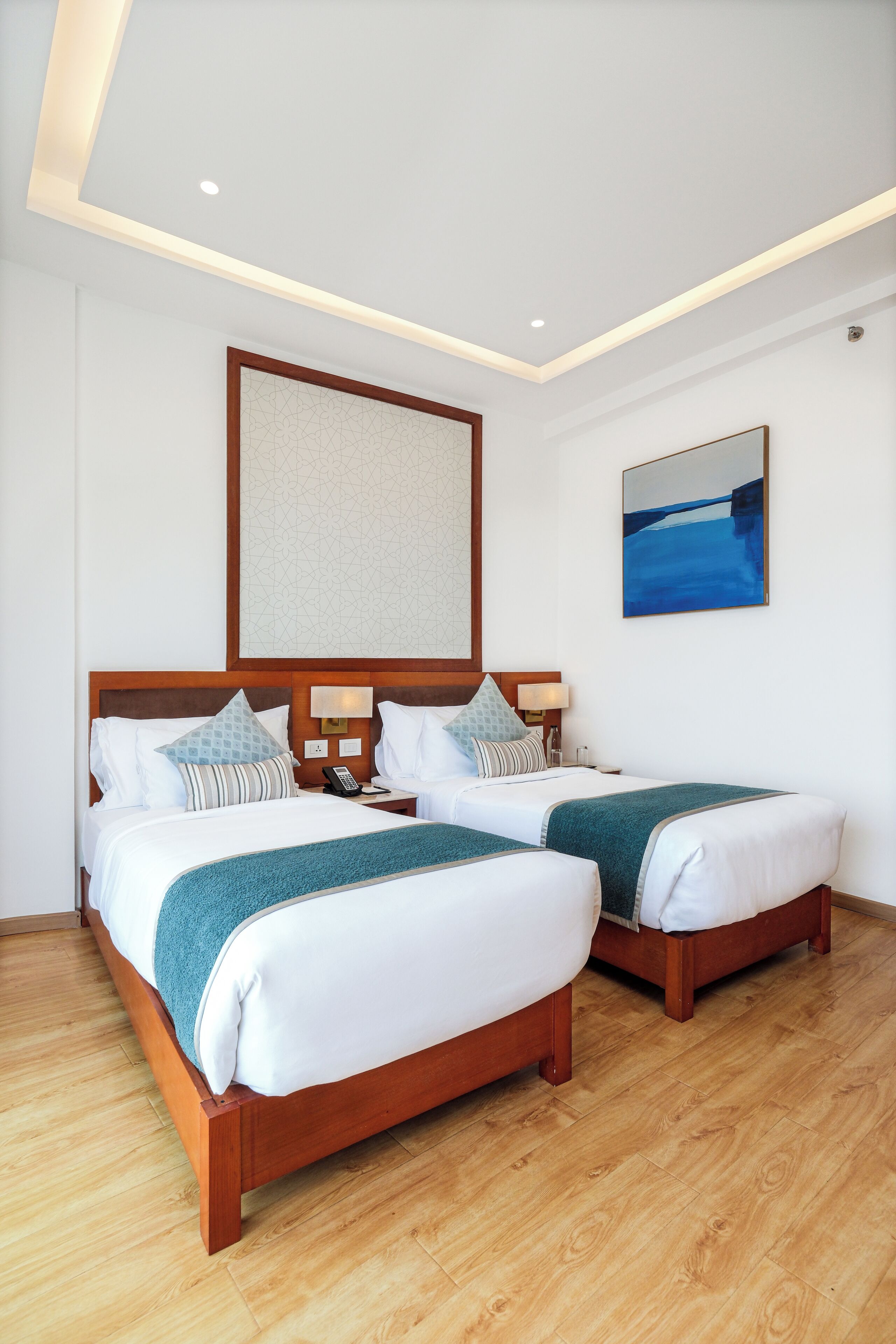 A hotel room with two beds, wooden headboards, a large abstract painting, and a view of the sea.