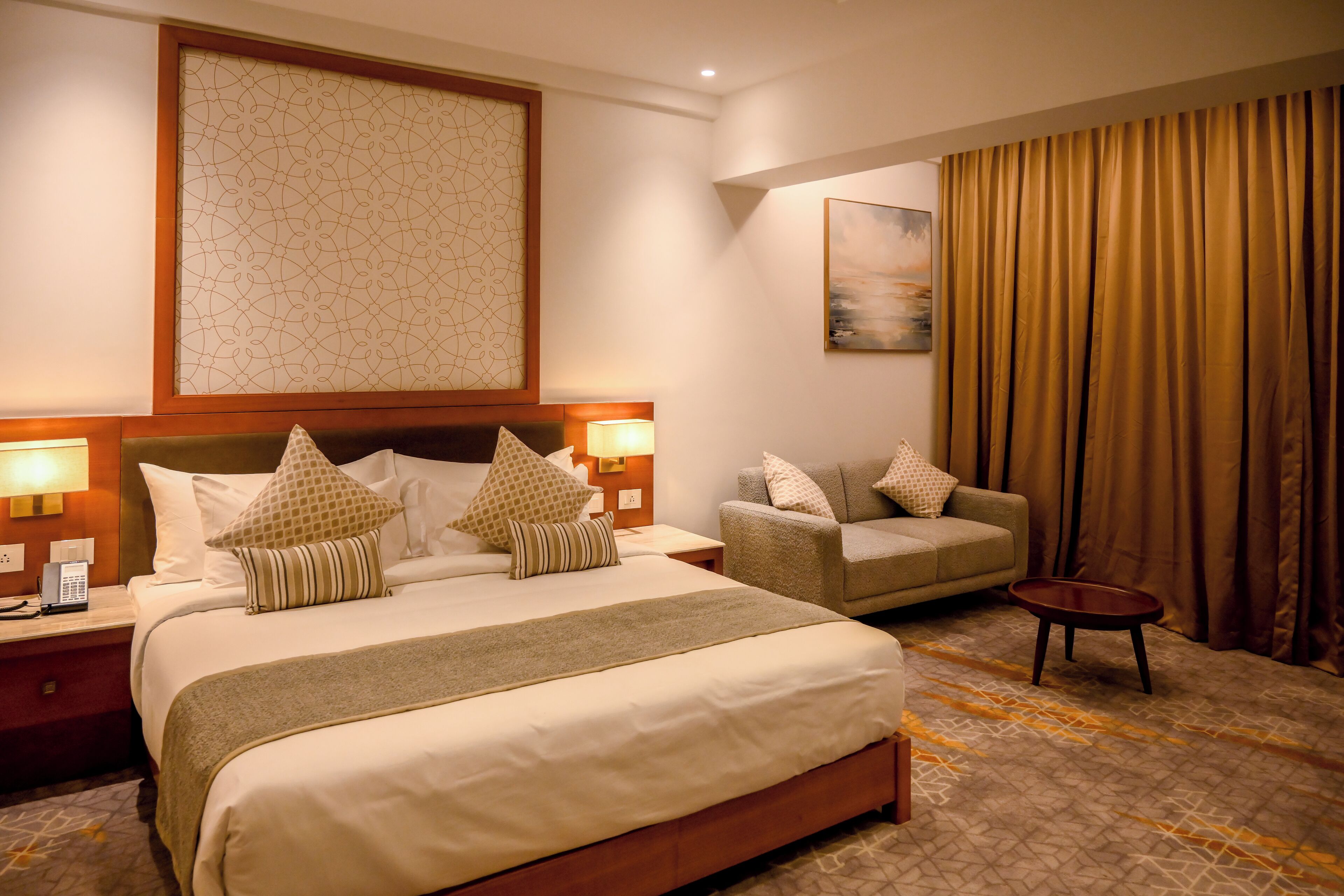 A hotel room with a large bed, a sofa, a small table, and a painting on the wall.