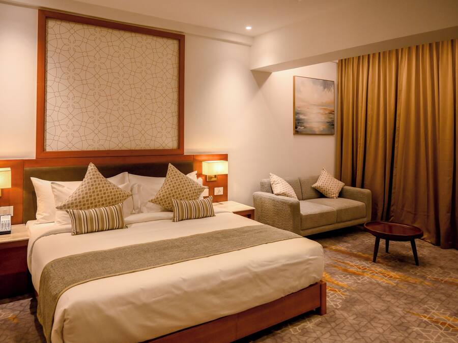 A hotel room with a large bed, a sofa, a small table, and a painting on the wall.