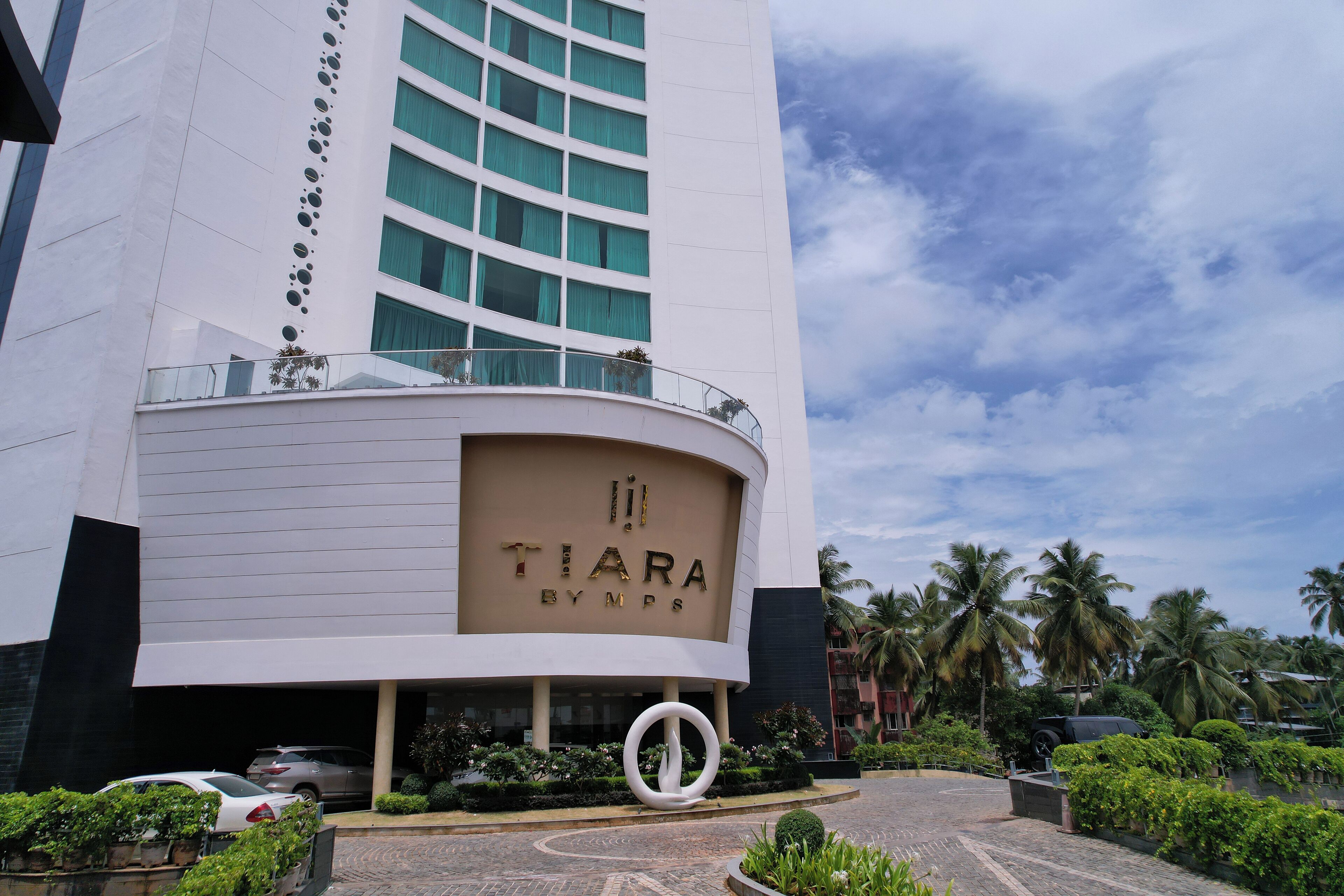 A modern hotel with a curved facade, a prominent entrance with a circular design element, and a view of palm trees in the background.
