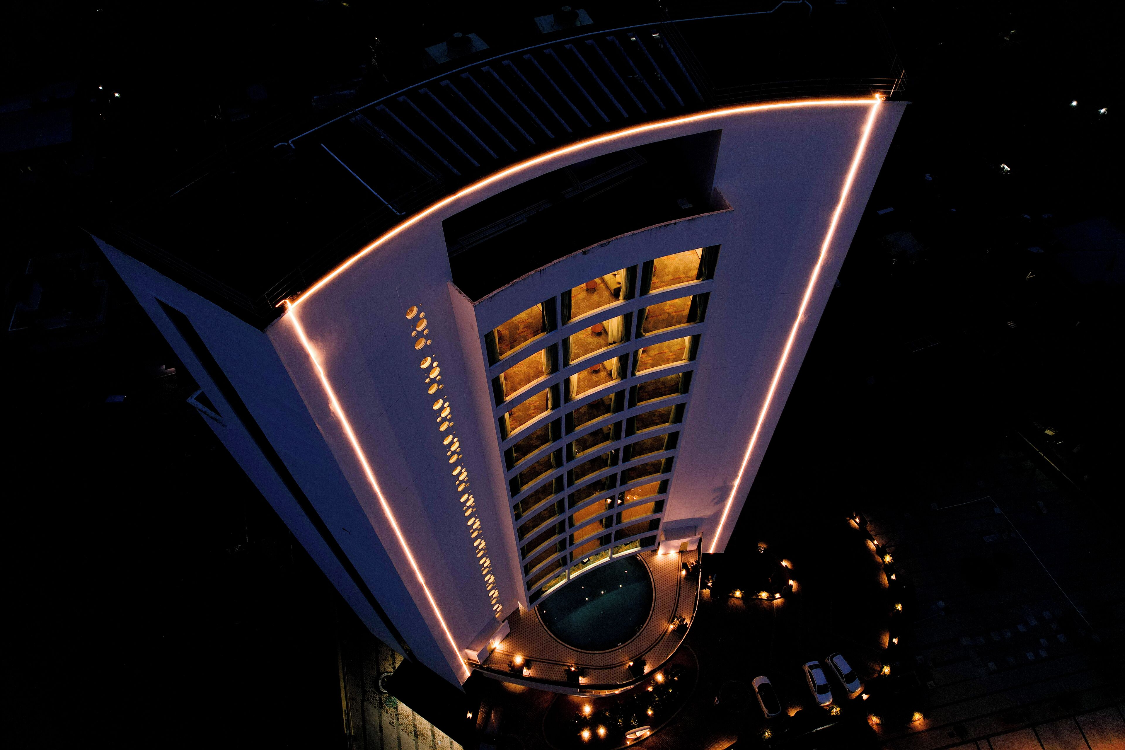 A modern hotel with a curved facade, multiple balconies, and a central courtyard with seating.