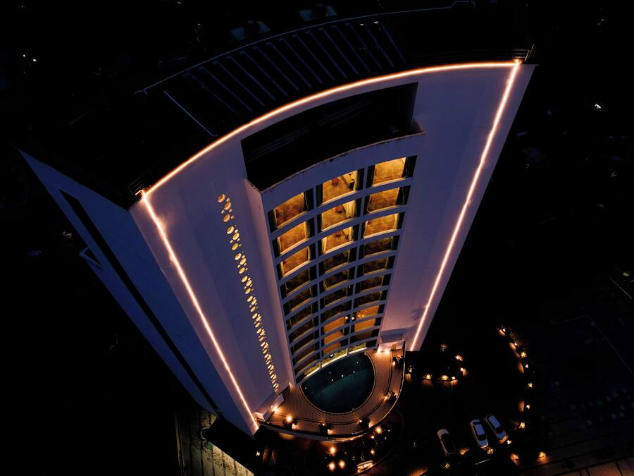 A modern hotel with a curved facade, multiple balconies, and a central courtyard with seating.