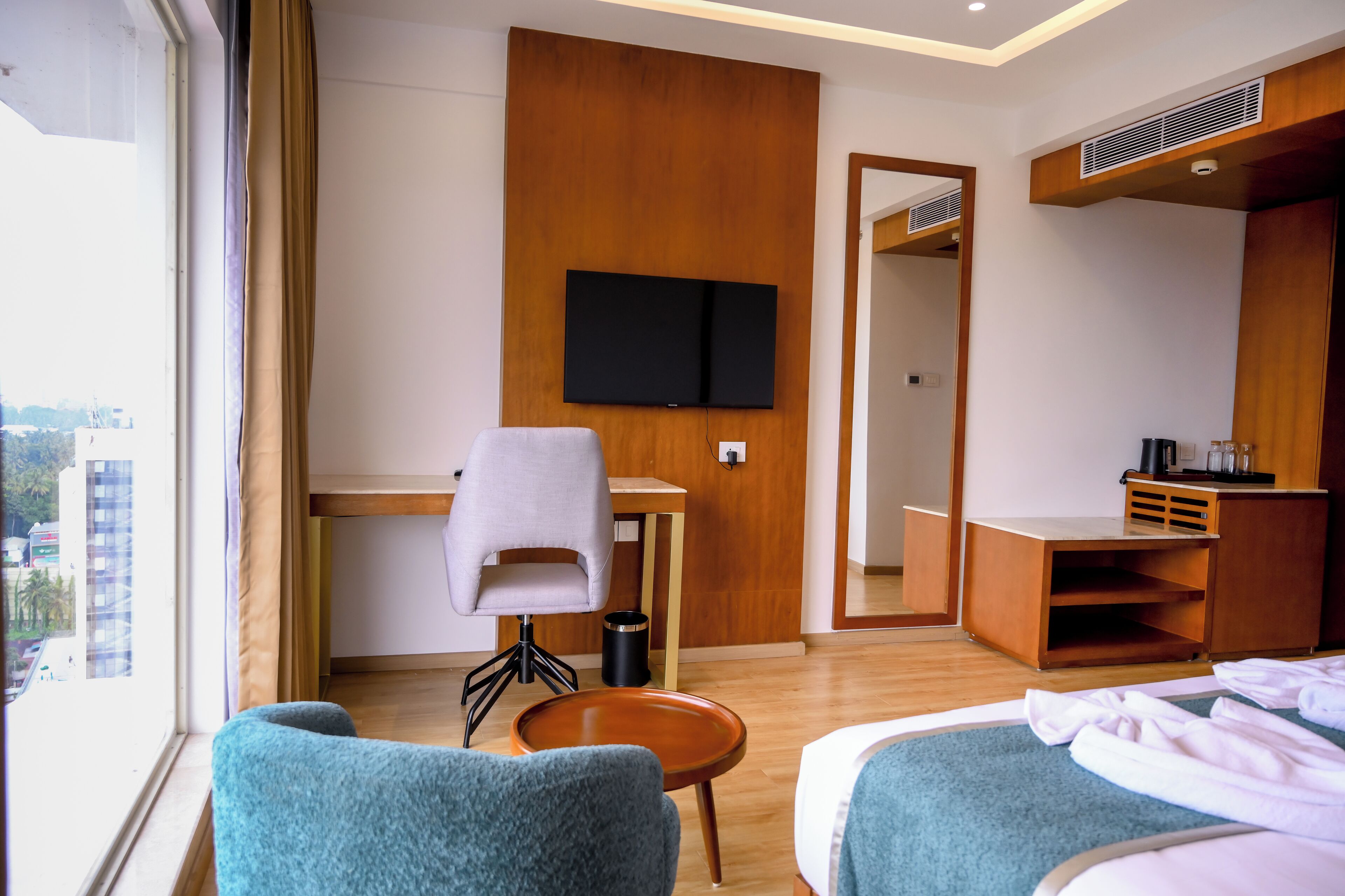 A hotel room with a bed, two chairs, a desk, a television, and a view of the city.