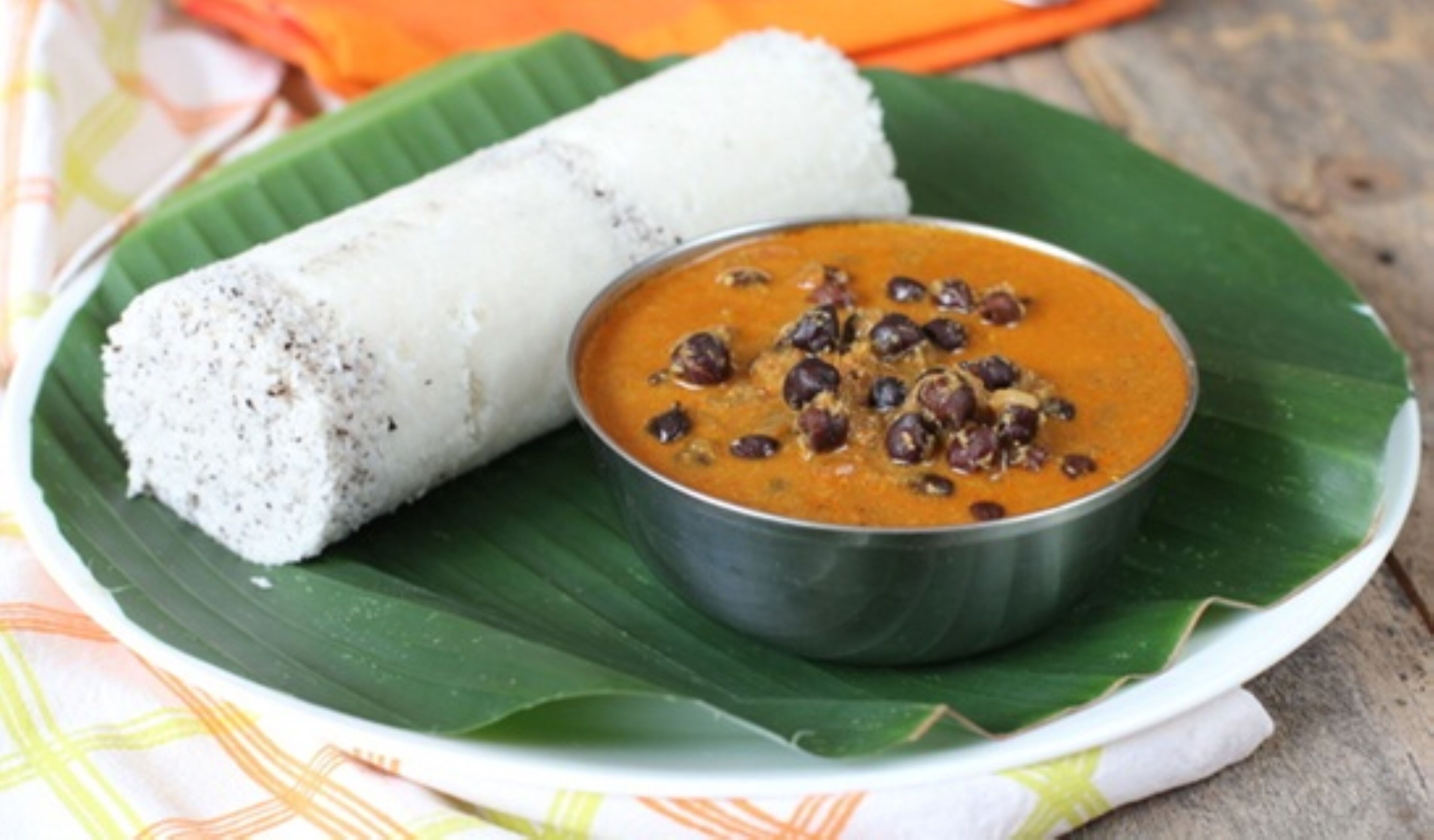 A plate with a rolled food item and a bowl of sauce with beans on a banana leaf.