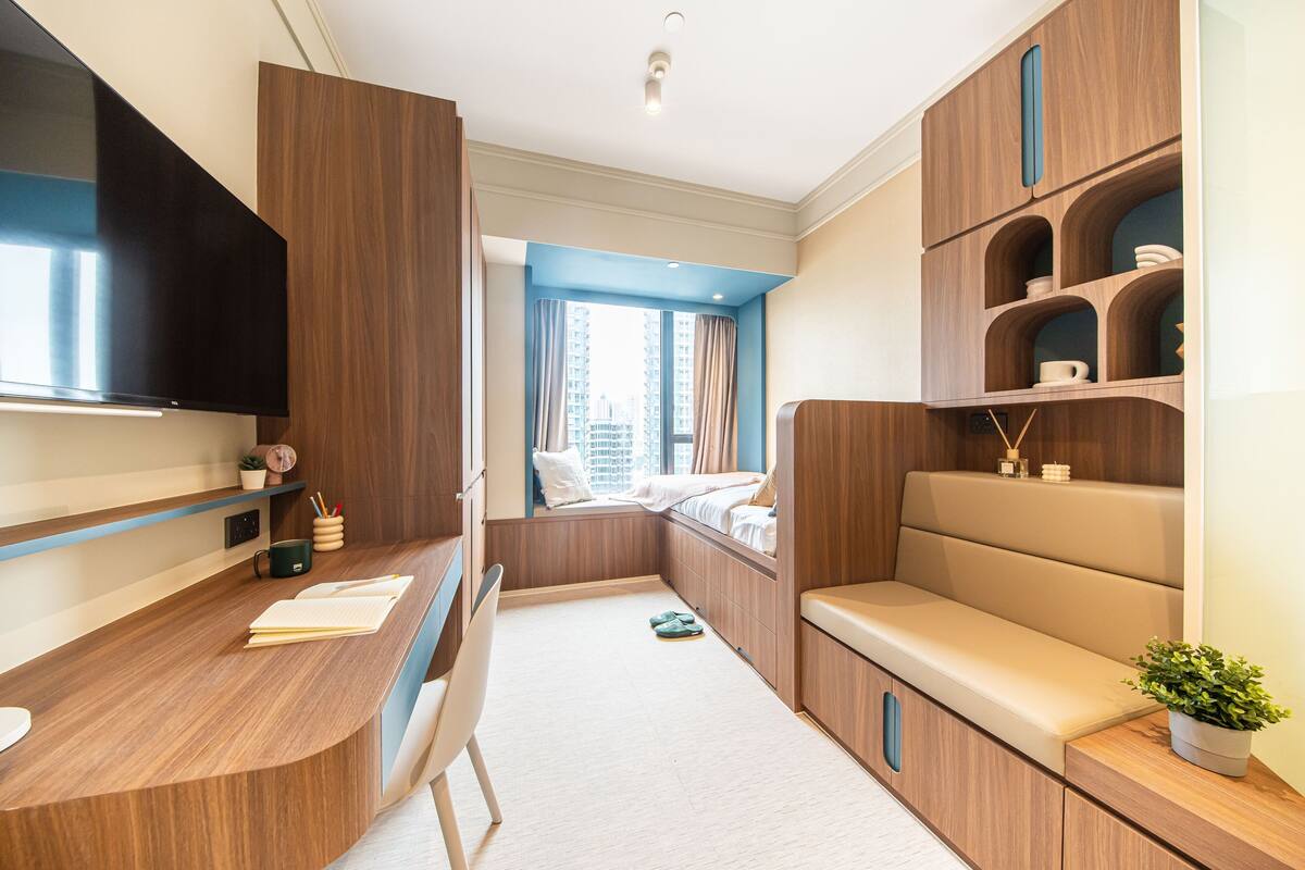 Una habitación de hotel moderna con un escritorio de madera, un televisor de pantalla plana, un área de descanso acogedora y un ventanal con cortinas.