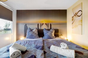 Una habitación de hotel con cama, almohadas, un cuadro en la pared y una ventana.