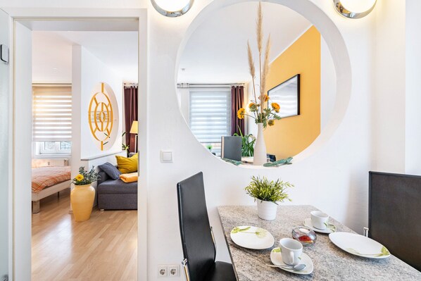 Un comedor moderno con un espejo redondo, una mesa de comedor con platos, tazas y una planta en maceta.
