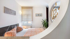 Un dormitorio moderno con una cama, un ventanal con persianas, una obra de arte colgada en la pared y una planta en maceta.