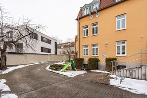 A residential building with a brick pathway, a green playground, and a staircase leading to an entrance.