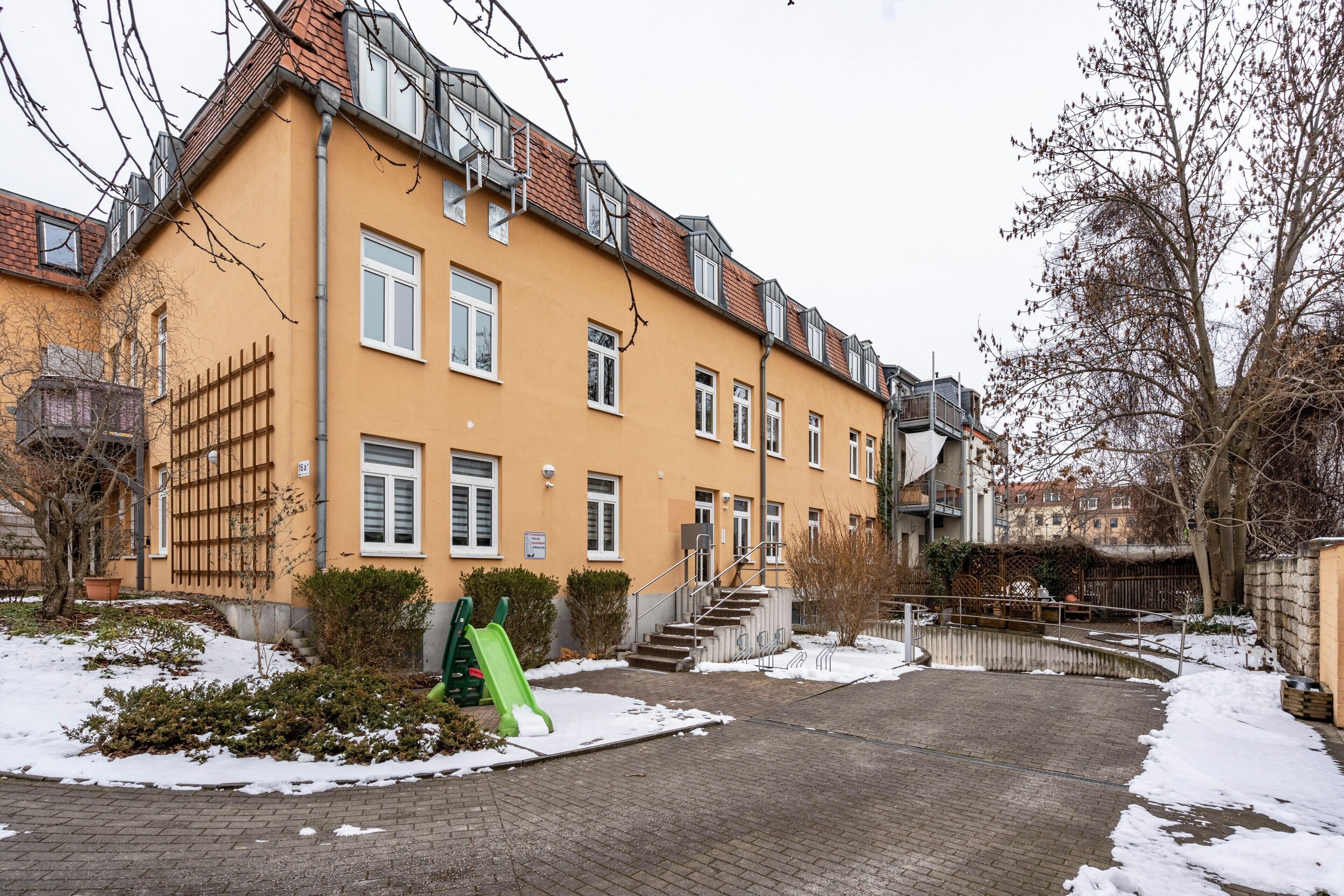Ein mehrstöckiges Wohngebäude mit Ziegelverkleidung, einer grünen Rutsche und verschneitem Gelände.