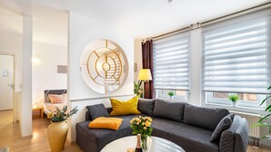Una sala de estar moderna con un sofá gris, cojines amarillos, una mesa redonda de centro y una gran obra de arte abstracto en la pared.