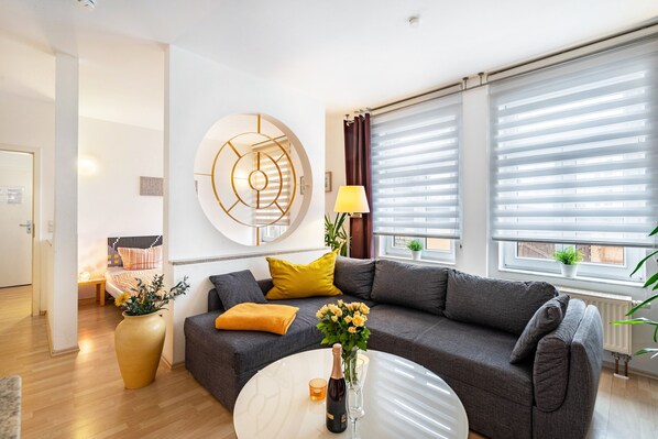 A modern living room with a grey sofa, yellow cushions, a round coffee table, and a large abstract wall art piece.
