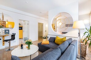 A modern living room with a grey sofa, a round coffee table, and a dining area with yellow cabinets.
