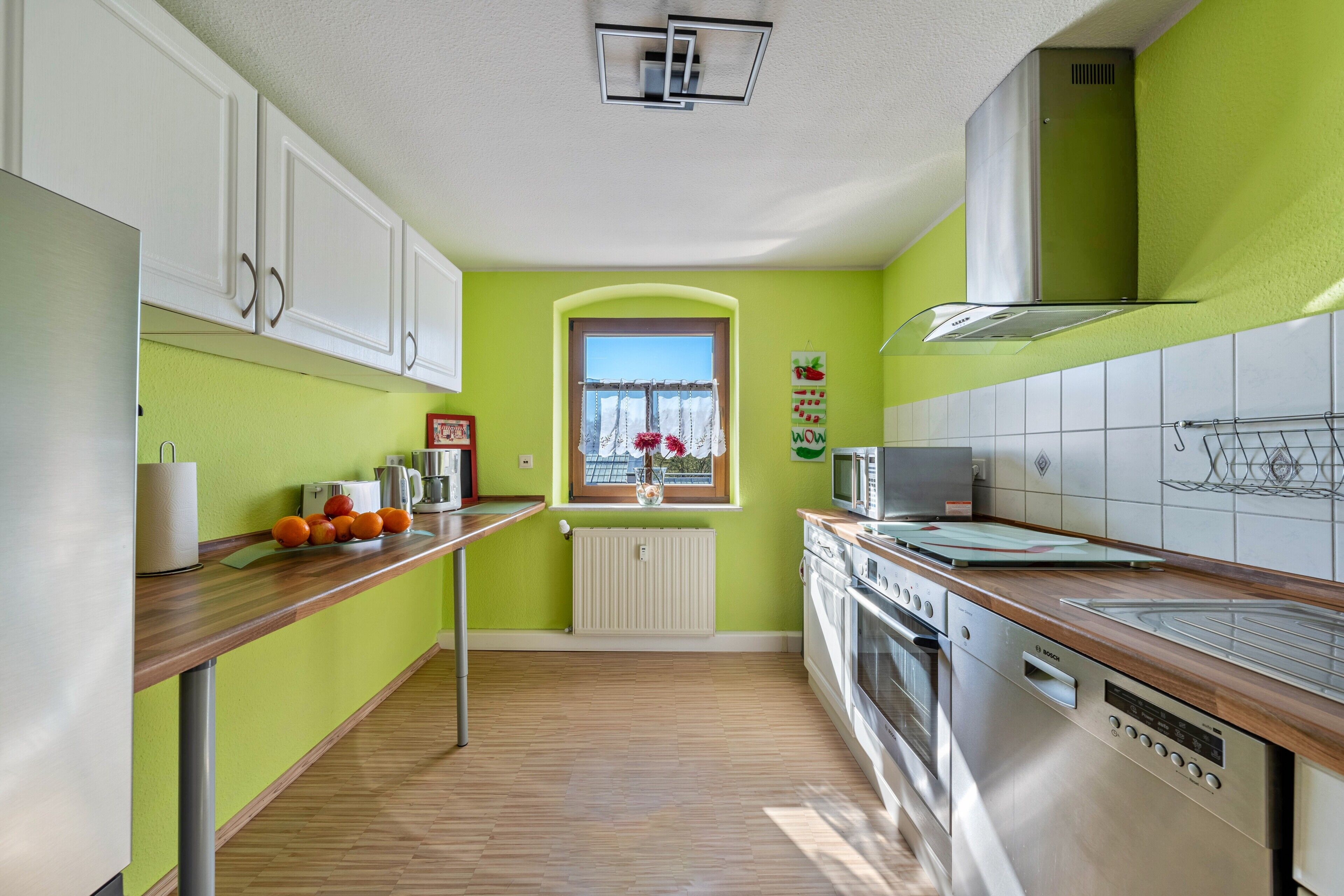 Una cocina con armarios blancos, encimera de madera, ventana con vistas y electrodomésticos de acero inoxidable.