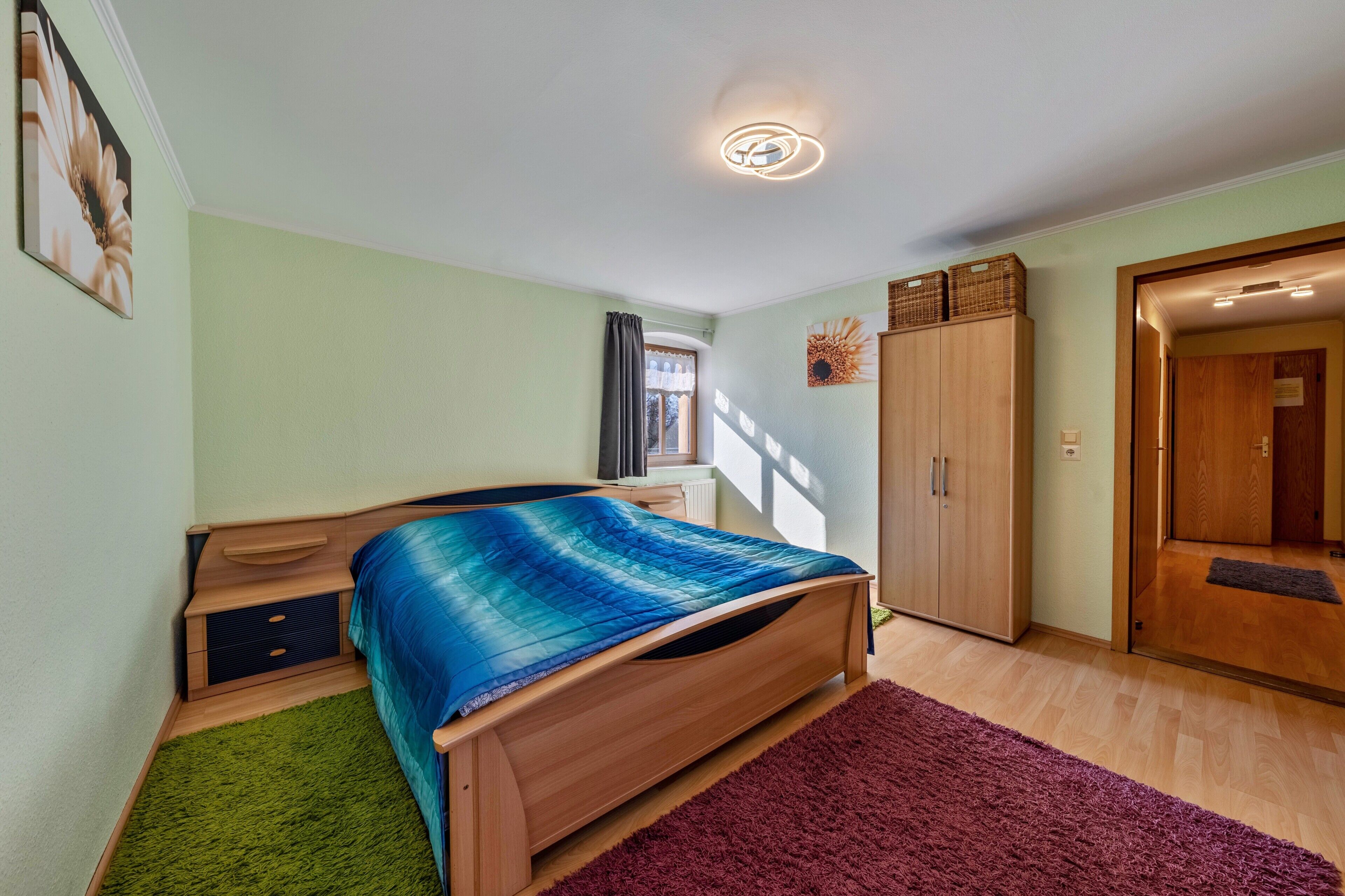Ein Schlafzimmer mit Bett, Kleiderschrank, Heizkörper und einer Tür zu einem anderen Raum.