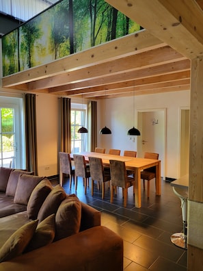 Un interior moderno con zona de comedor, vigas de madera en el techo y un gran ventanal con cortinas.