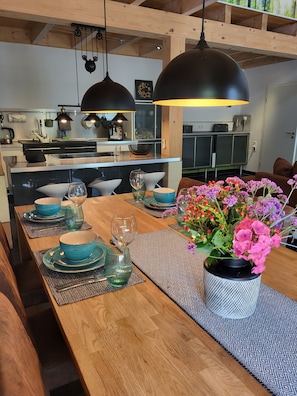 Cozinha moderna com vigas de madeira, luminárias pendentes e um espaço de refeições com uma mesa de madeira posta para quatro pessoas.