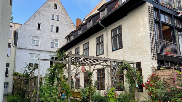 Ein Garten mit einem Fahrrad, einer Pergola und einem Gebäude mit zahlreichen Fenstern und Balkonen.