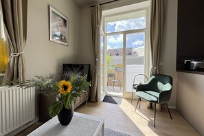 A room with a radiator, a black TV, a green chair, a large window with curtains, and a framed picture on the wall.