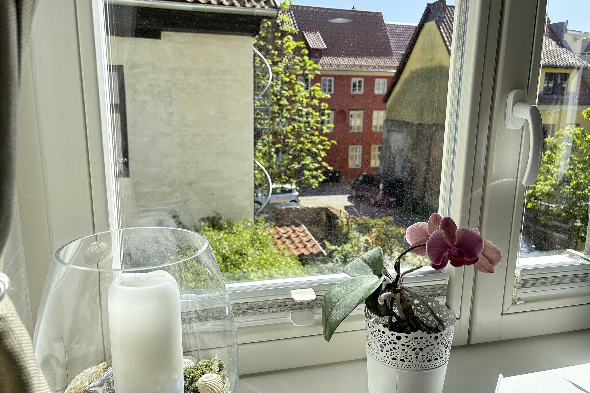 Een raam met een pot orchidee, een glazen vaas en een klein decoratief object op de vensterbank.