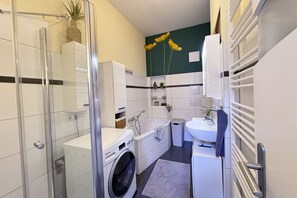 Une salle de bain compacte dotée d’une douche à parois de verre, d’un lave-linge, d’une baignoire et d’un lavabo.
