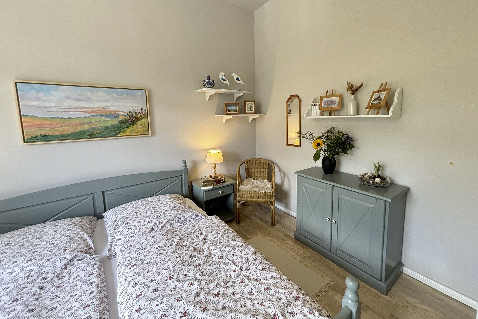 Ein Schlafzimmer mit Bett, Sessel, Nachttisch, Kommode und Wandregalen mit Dekoration.