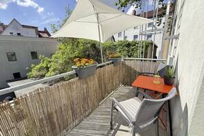 Un balcon avec une table, des chaises, des plantes en pot et un grand parasol.