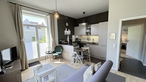 Ein gemütlicher Wohnbereich mit einer Couch, einem kleinen Esstisch, einem Fernseher, einer Küchenzeile und einer Schiebetür nach draußen.