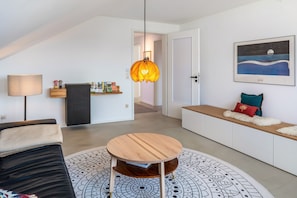 Un salon moderne avec une table basse ronde en bois, un canapé, une lampe suspendue, une bibliothèque et un tableau au mur.