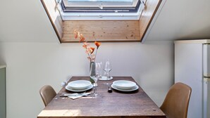 A dining table with plates, glasses, and a vase with flowers, under a skylight.