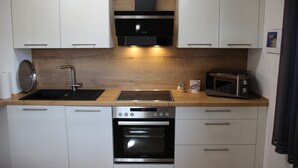 Una cocina moderna con armarios blancos, una estufa de acero inoxidable, horno empotrado, microondas y encimera de madera.