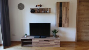 Una sala de estar moderna con un televisor de pantalla plana sobre un soporte de madera, un reloj en la pared y un mueble de madera.