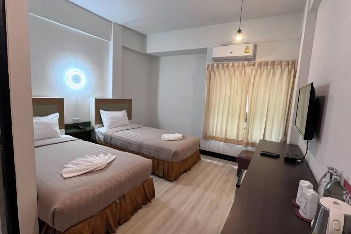 Quarto de hotel com duas camas, uma escrivaninha, televisão e ar condicionado.